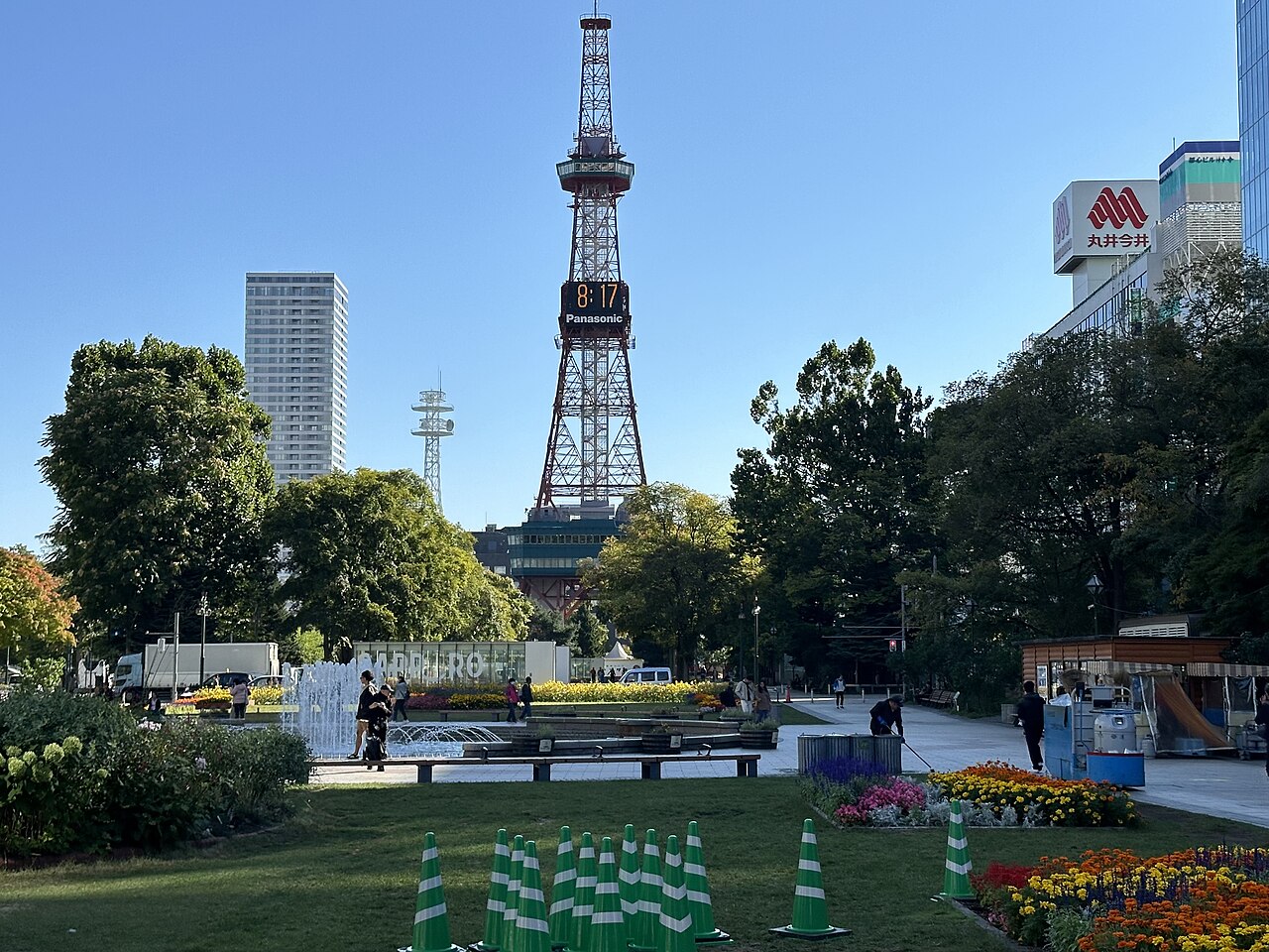 Czerwona Sapporo TV Tower z zegarem cyfrowym nad trawnikiem i klombami wschodniej części parku Odori, wrzesień 2024.
