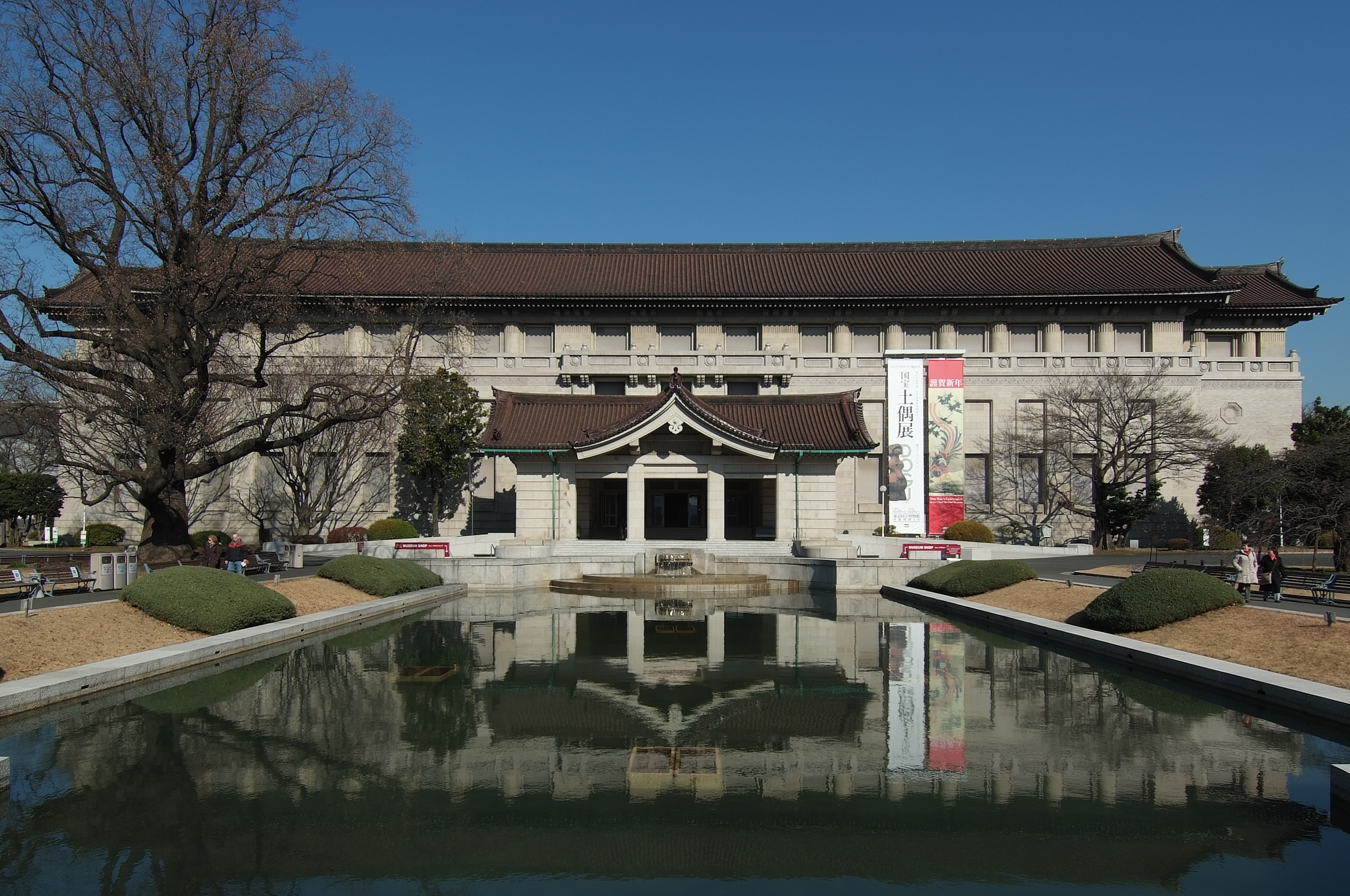 Fasada Honkan Tokyo National Museum ze stawem przed budynkiem; ujęcie 2010 — staw ma zostać zamieniony w trawnik do 2027 r., zdjęcie nie pokazuje aktualnej wystawy ani kolejki do kas.